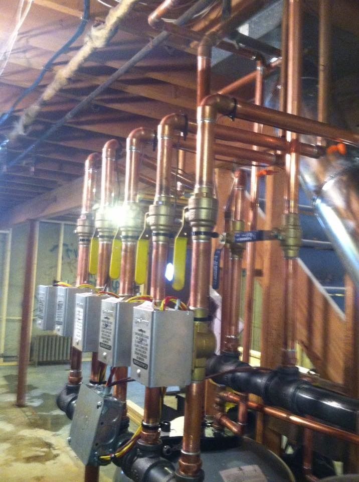 Copper pipes and valves with yellow handles in a mechanical room, connected to black equipment.