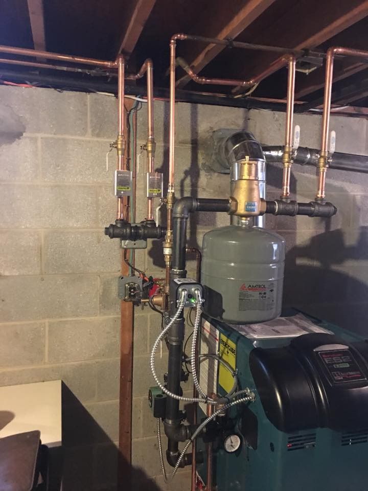 Copper pipes and boiler system against a concrete block wall in a basement.