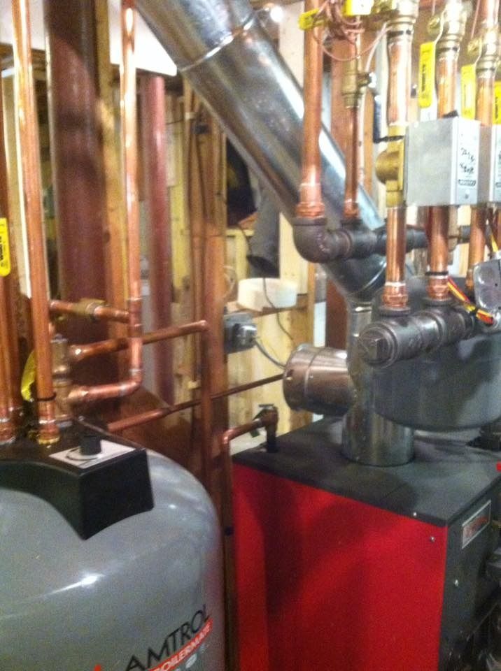 Copper pipes and a boiler in a mechanical room. A red-cased boiler is next to a silver tank and pipes.