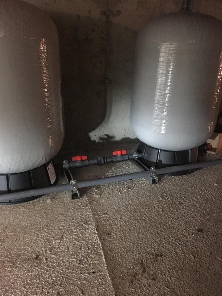 Two white water pressure tanks connected by pipes and valves, set on a textured concrete floor.