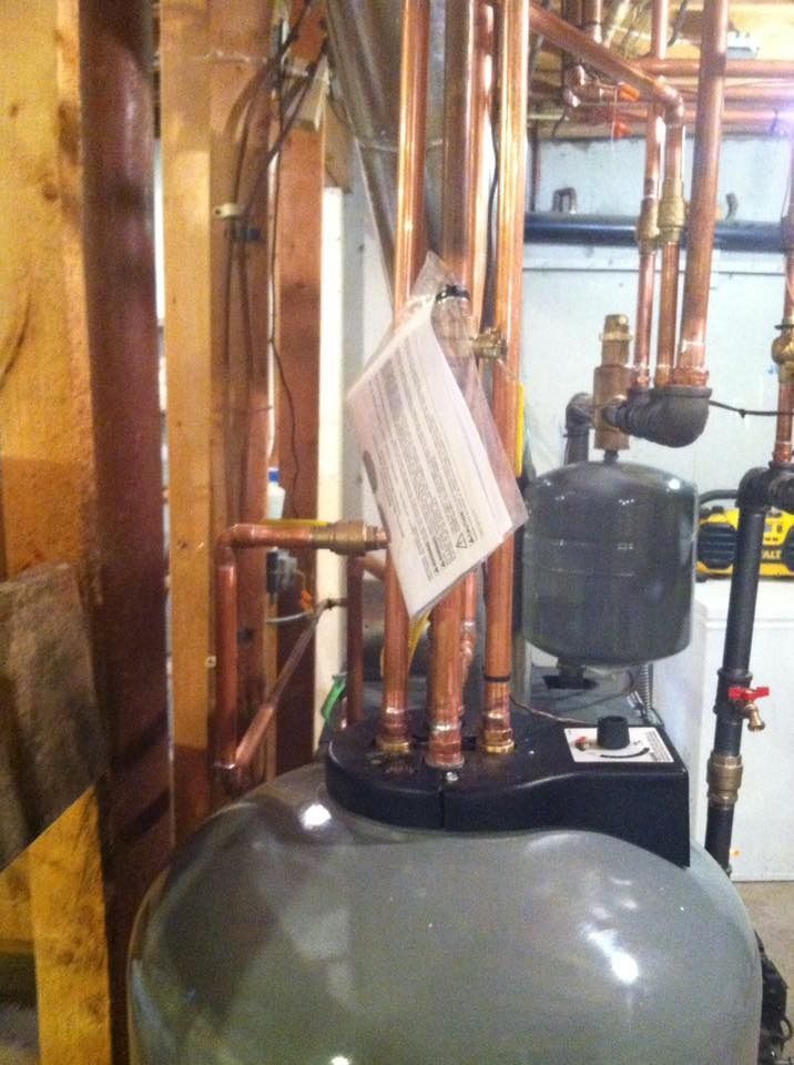 Copper pipes connected to a gray water heater tank in a basement setting.