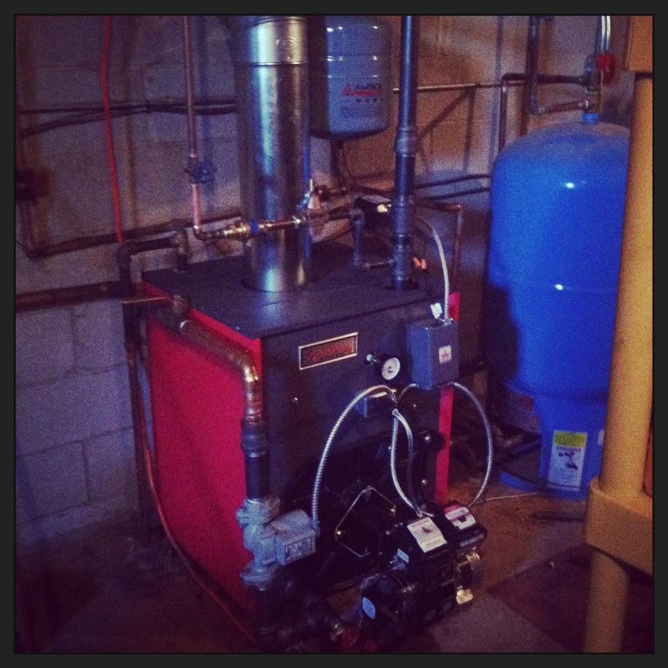 A red and black boiler with connected pipes and a blue water tank in a basement setting.