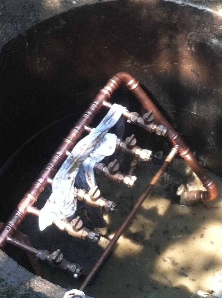 Copper pipe manifold in a dark, dirty pit, with valves and a cloth.