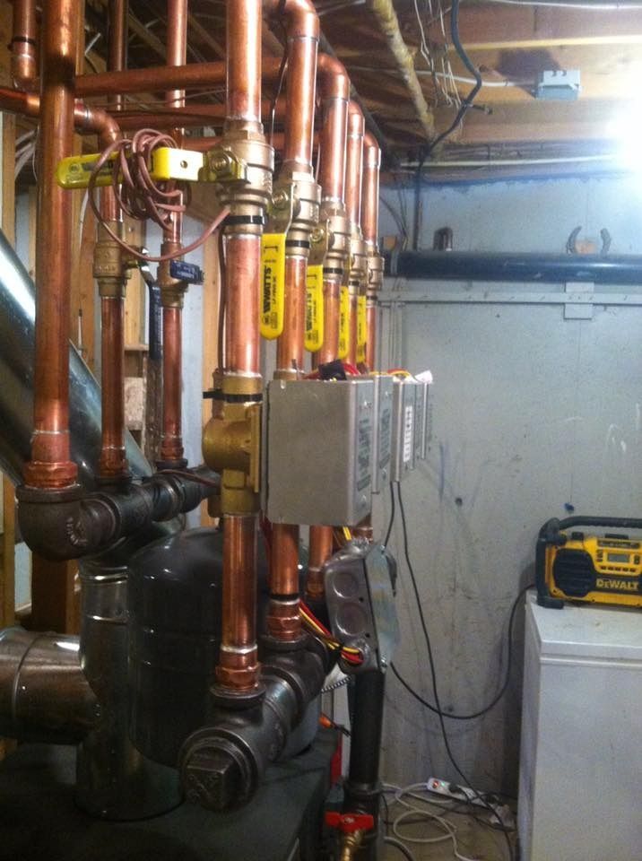 Copper pipes and valves, part of a heating system, against a light gray wall.