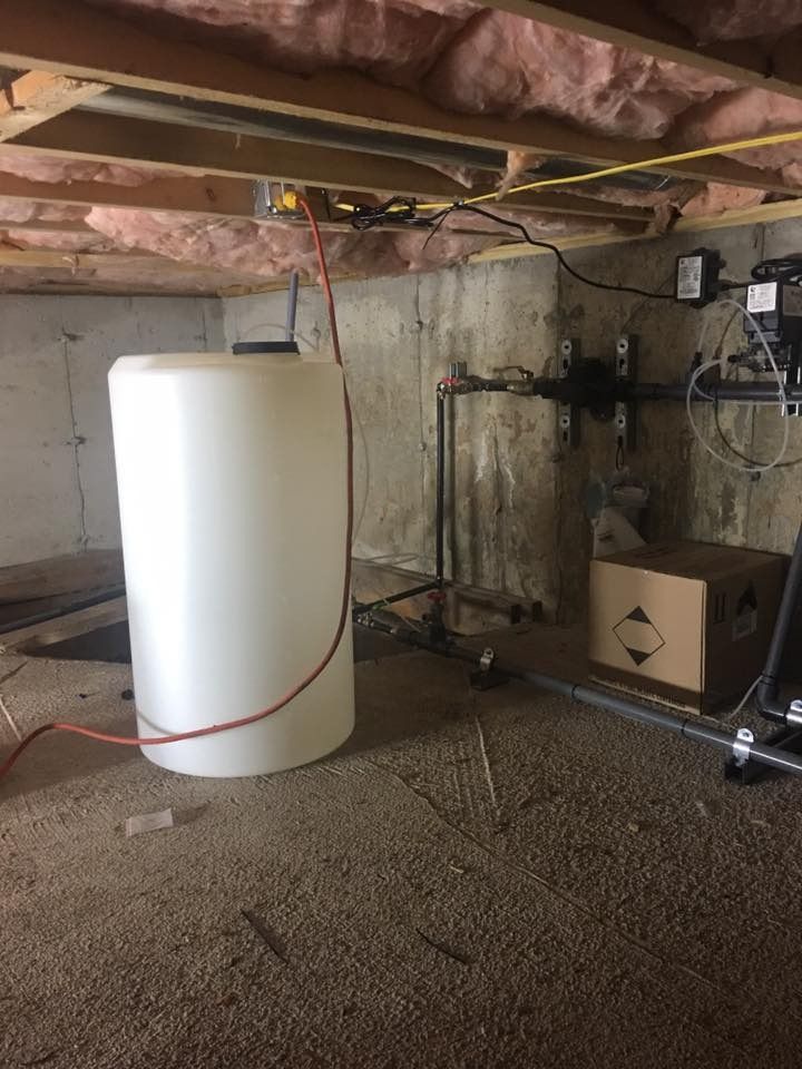 White water tank in a basement, red hose connected. Concrete and wood ceiling.