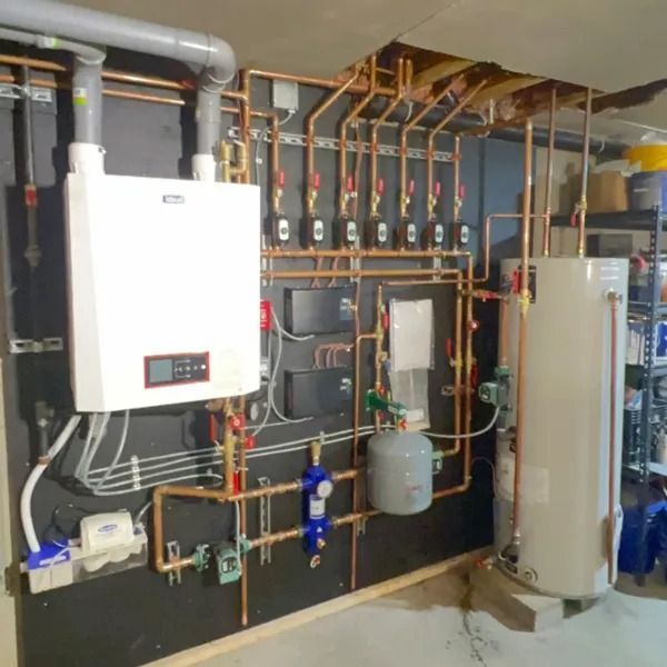 Copper pipes and white heating components against a black wall. Boiler and water tank with multiple valves.