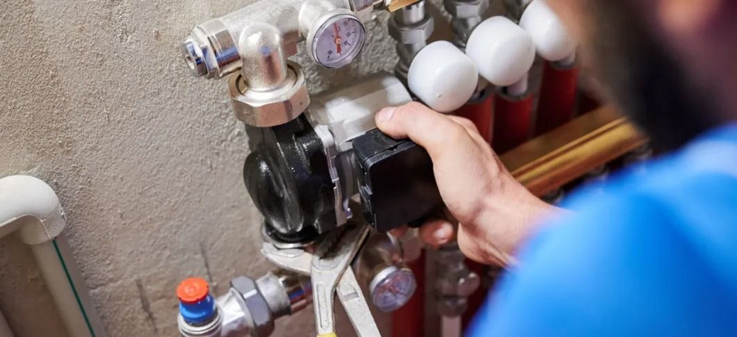 A person in a blue shirt is repairing plumbing equipment with a wrench.