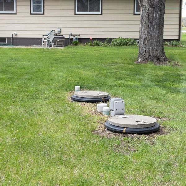 Lawn with two circular septic tank covers, a small electrical box, and a tree. A beige house is in the background.