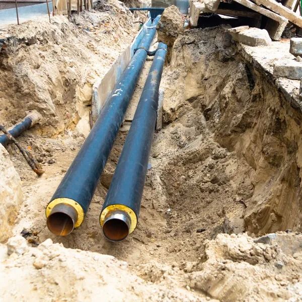 Pipes in trench, likely for underground utility work. Steel pipes with black insulation, dirt surrounds.