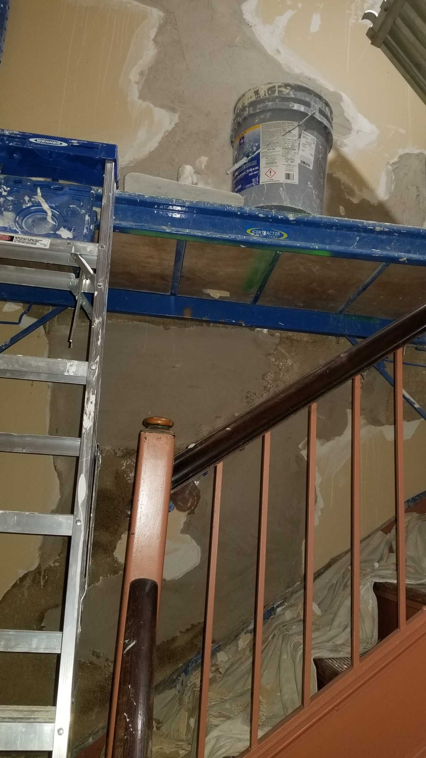 A ladder is sitting on top of a wooden railing next to a staircase.