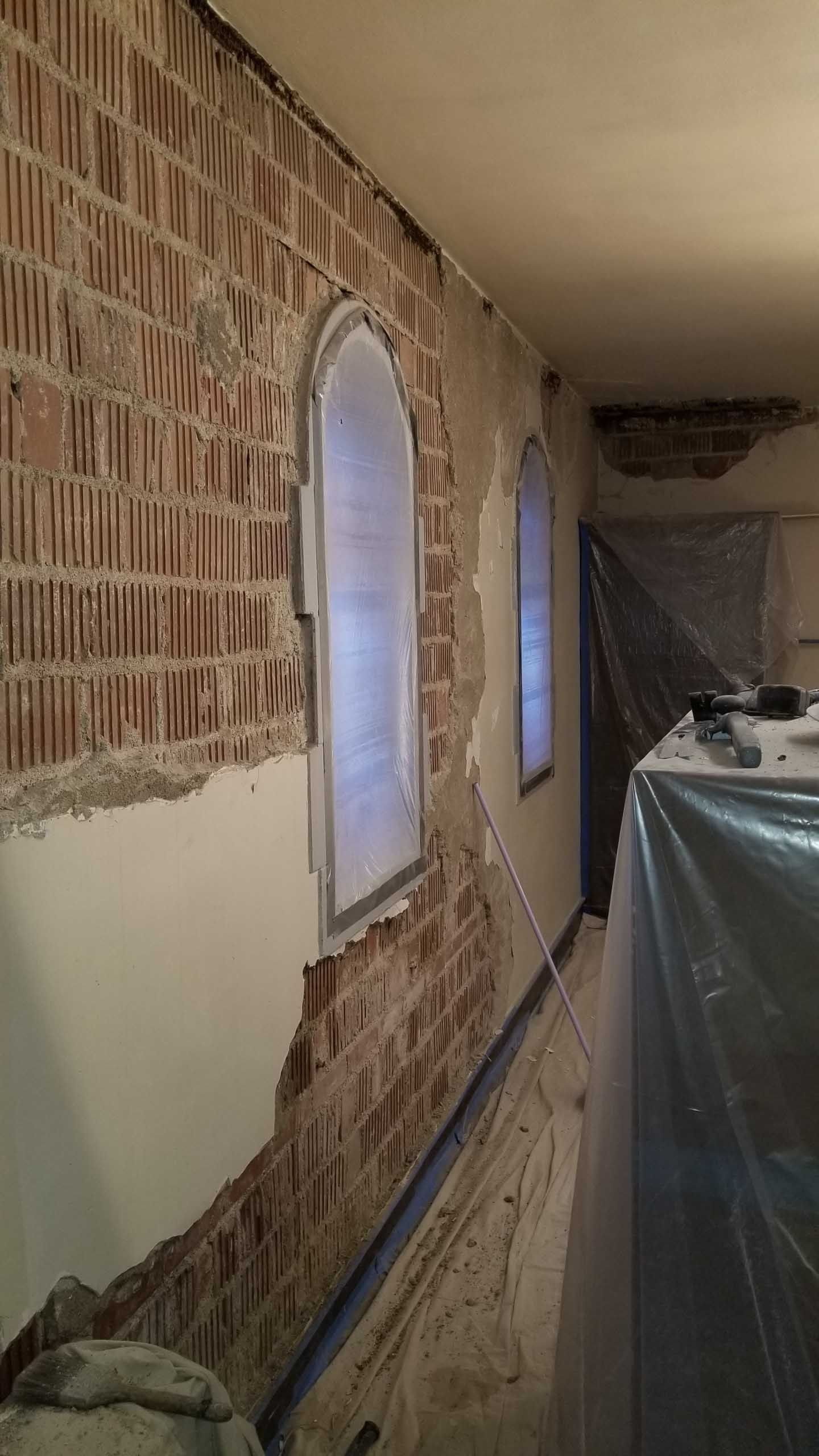 A brick wall with arched windows is being remodeled.