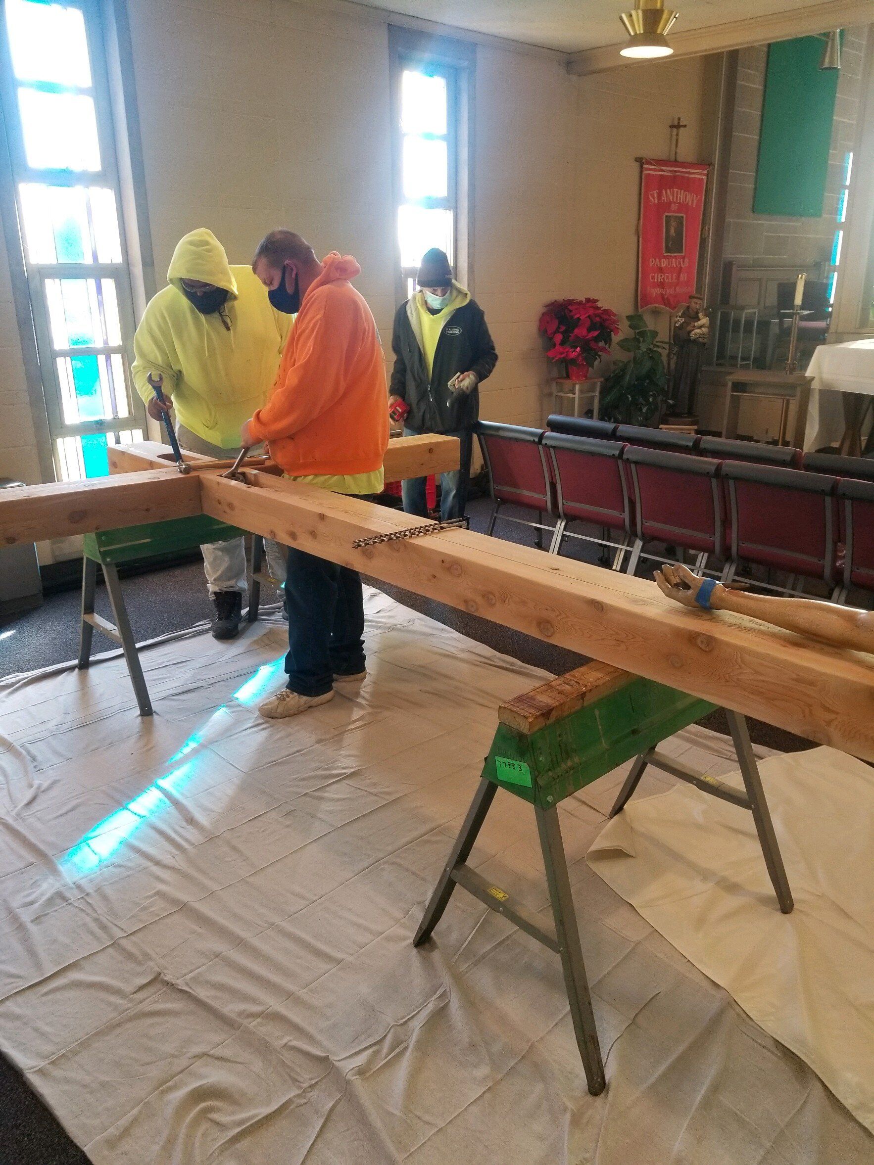 A group of people are working on a wooden beam in a room.