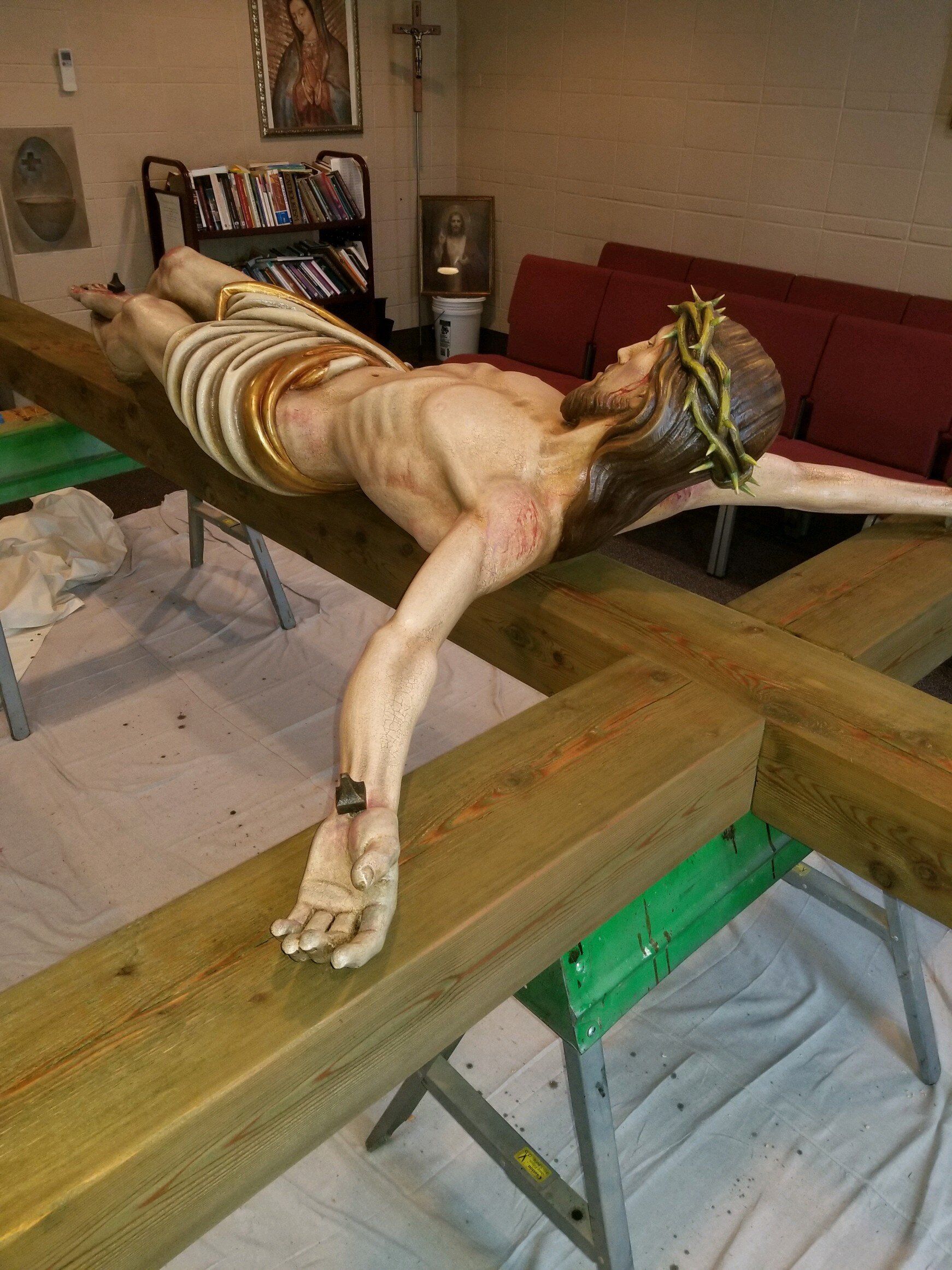 A statue of jesus is laying on a wooden cross in a room.