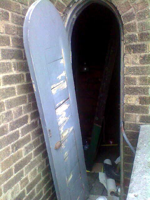 A blue door is open to a dark room in a brick building