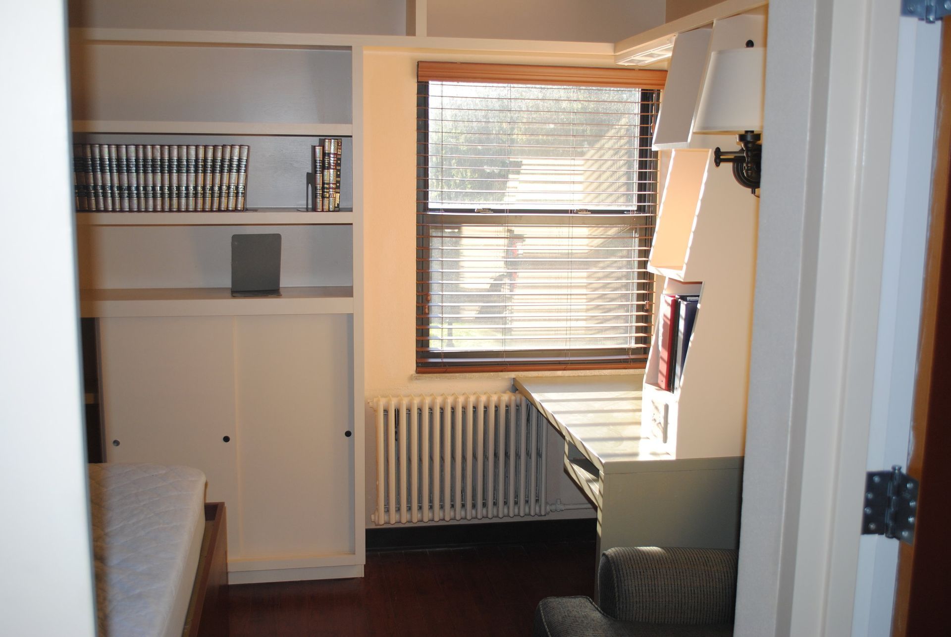 A bedroom with a desk and a window with blinds