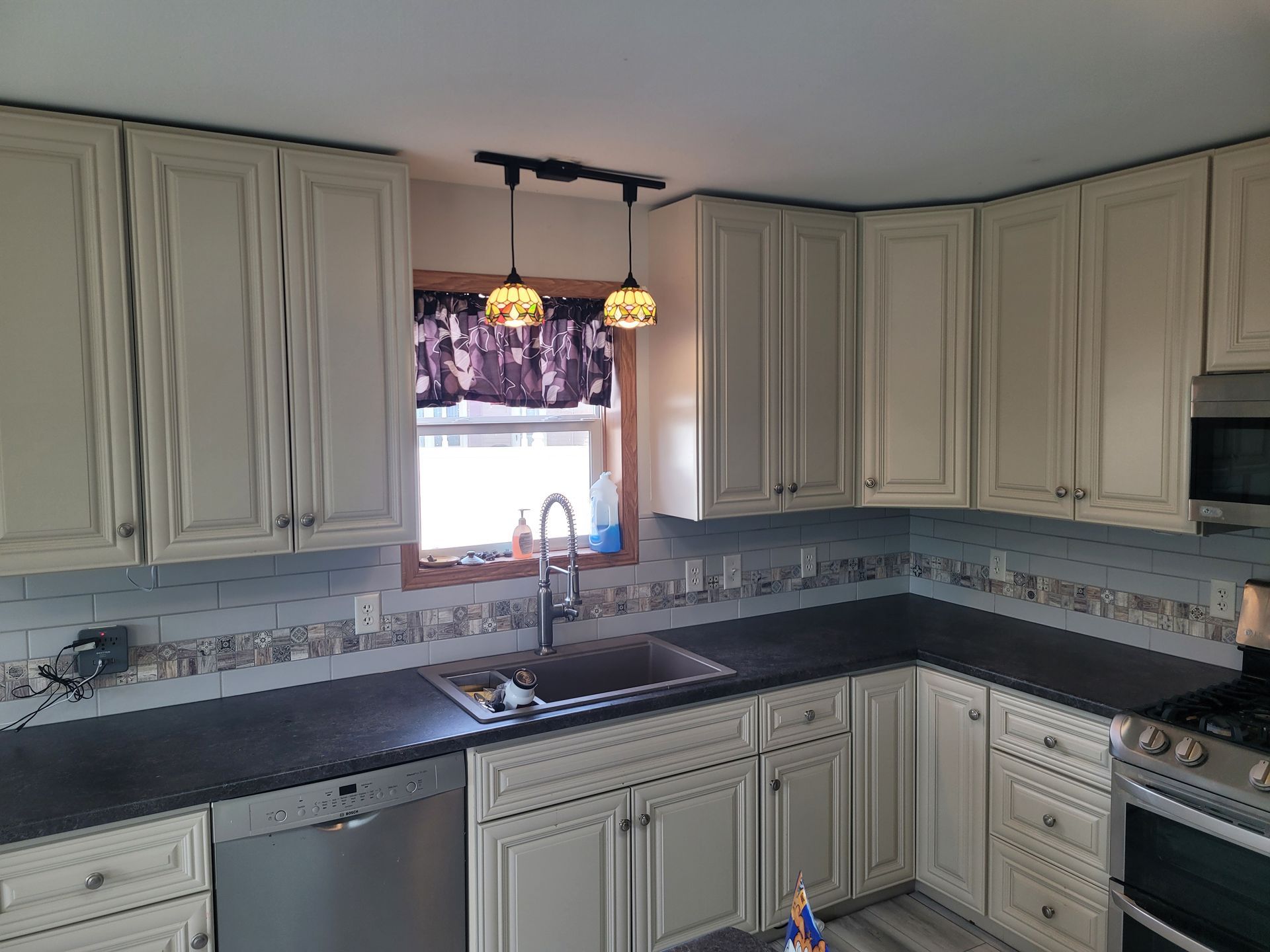 A kitchen with white cabinets , black counter tops , stainless steel appliances and a sink.