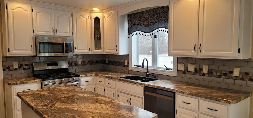 A kitchen with white cabinets , granite counter tops , stainless steel appliances and a large island.