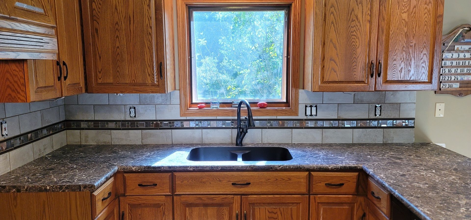 A kitchen with wooden cabinets , granite counter tops , a sink and a window.