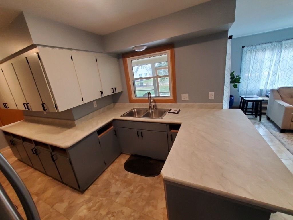 A kitchen with gray cabinets , a sink , and a window.