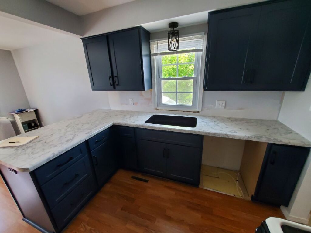 A kitchen with blue cabinets and white counter tops and a window.