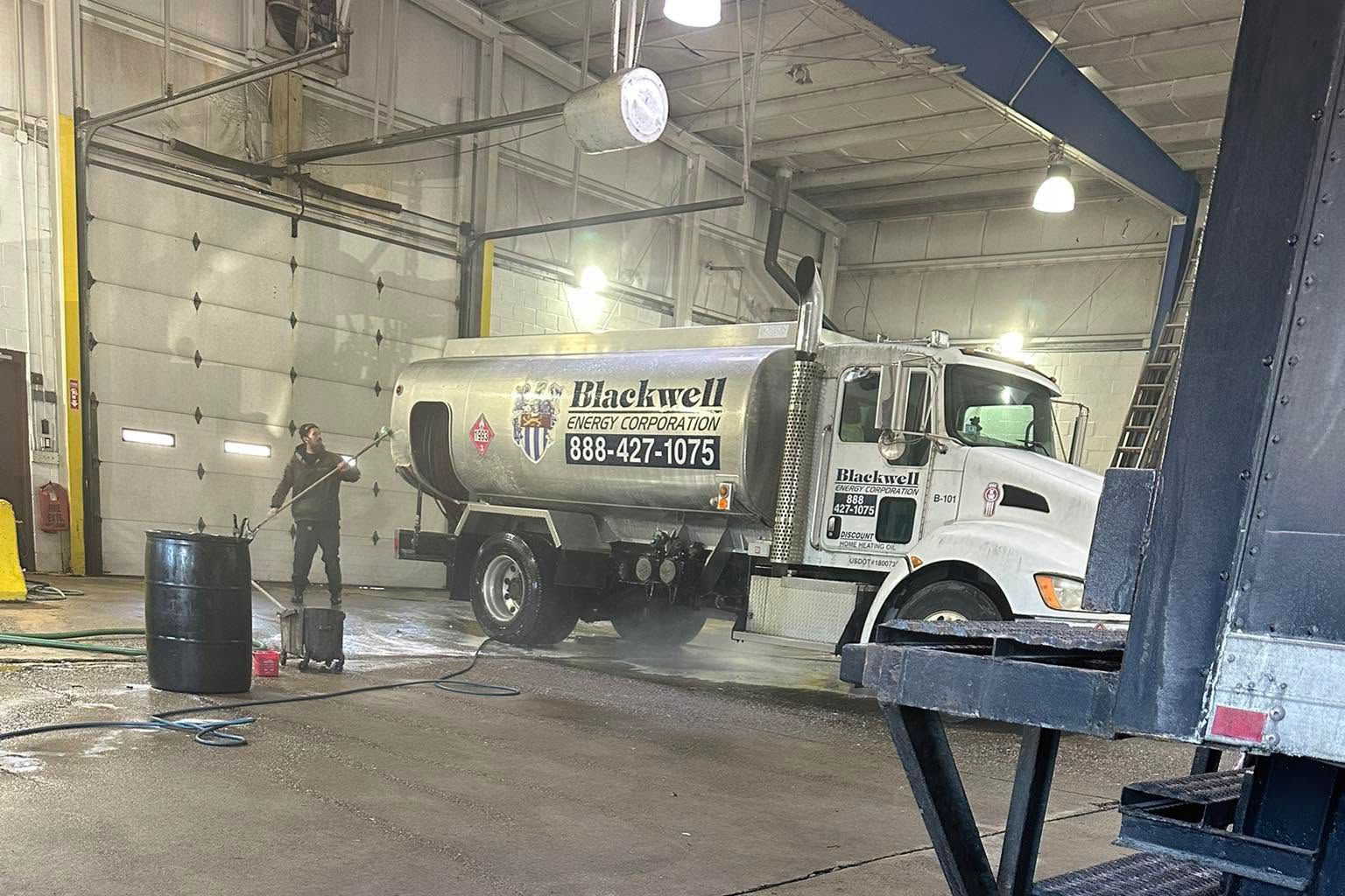 White Rockwell sewer truck inside a wet garage bay, with one worker near the rear.