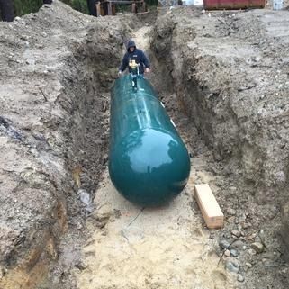 Worker handling a large teal tank in a dirt trench at a construction site