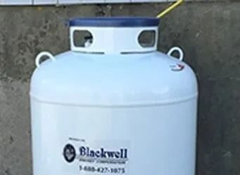 White Blackwell propane tank with blue top against a concrete wall