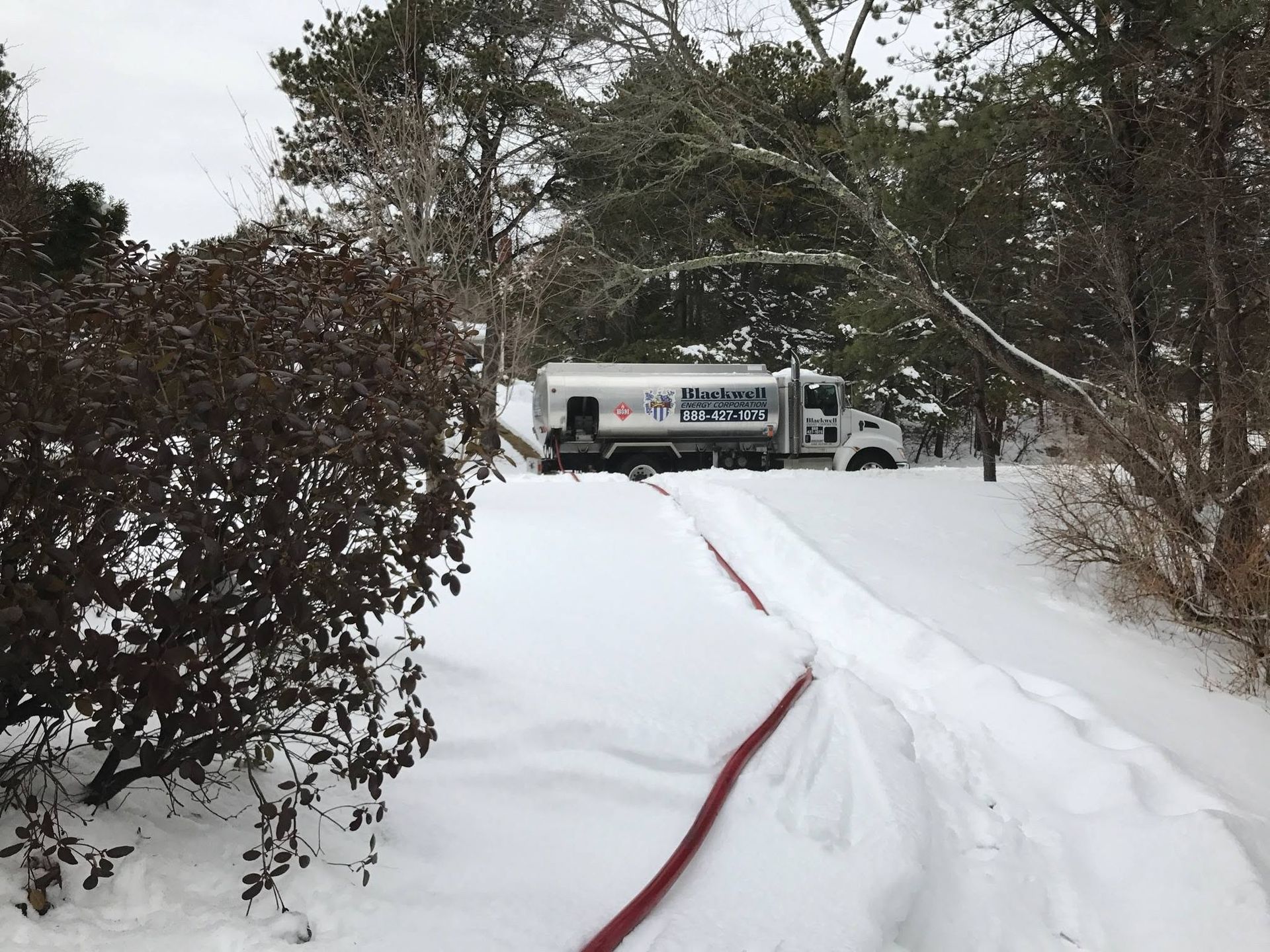 Snowy driveway with a red hose leading to a white truck in the background