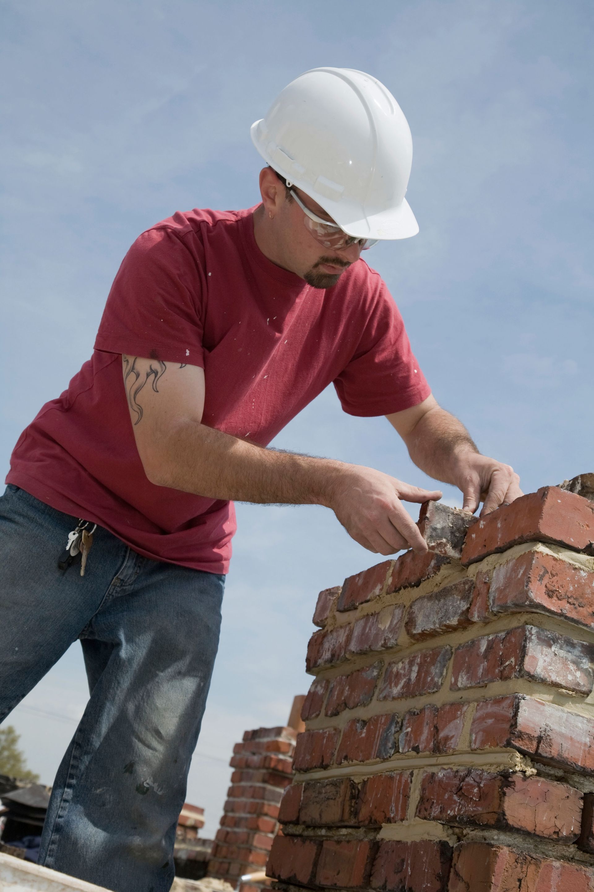 Construction worker in a white hard hat laying bricks on a brick wall outdoors