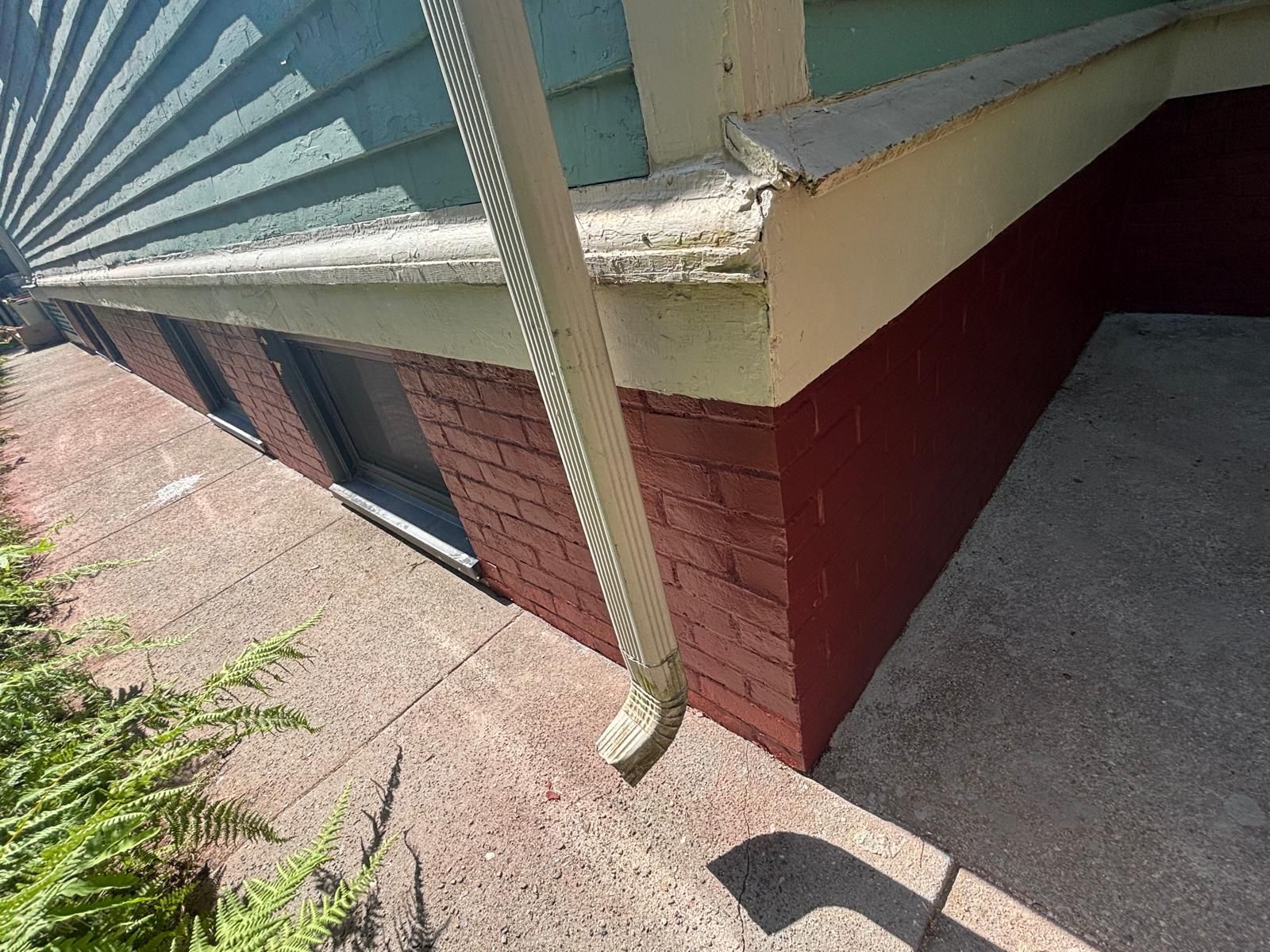 Red brick house foundation with white trim and a downspout