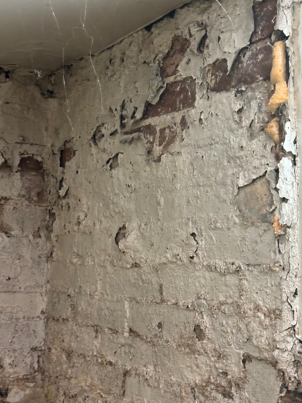 Corner of a brick wall with peeling, crumbling plaster.