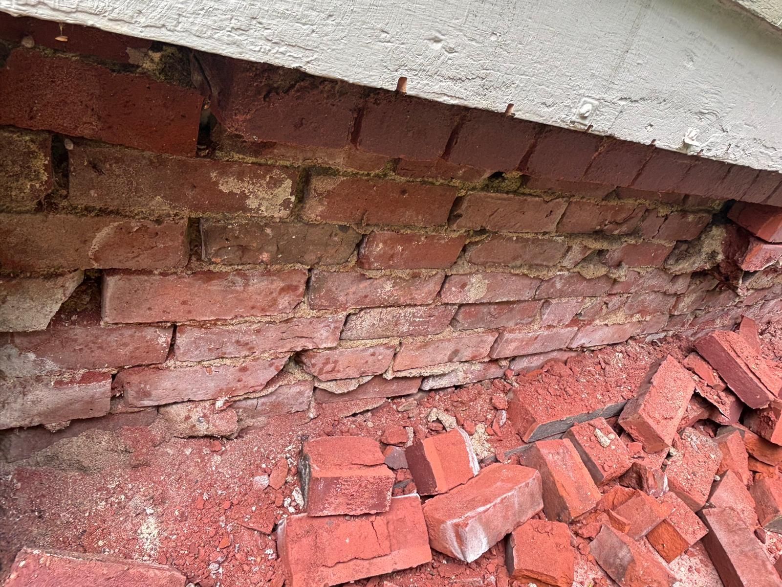 Damaged brick wall with fallen bricks; some mortar erosion.