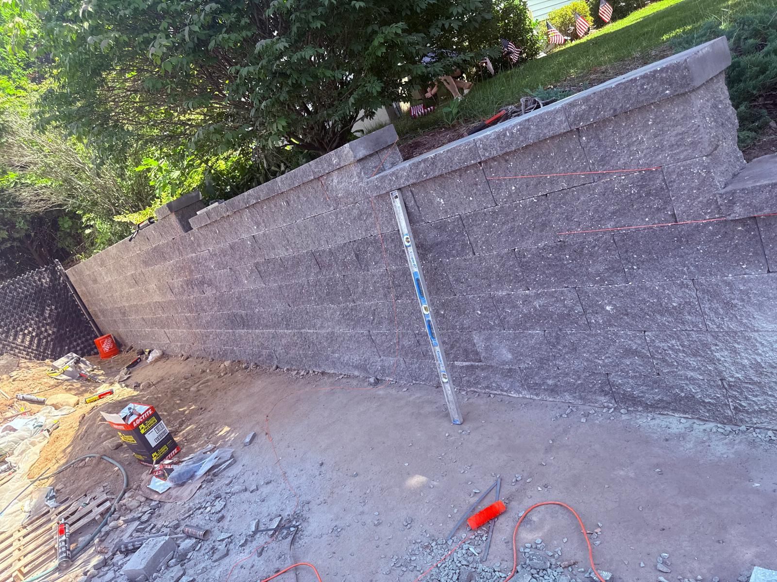 Retaining wall construction: Gray concrete wall, tools on ground, and a level in the work area.