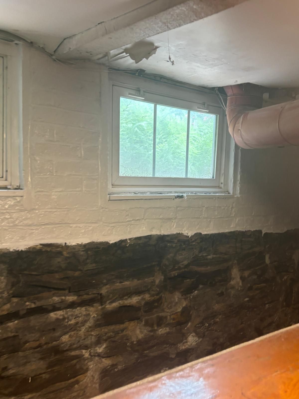 Basement with stone foundation, small window, painted white walls, and exposed ductwork.