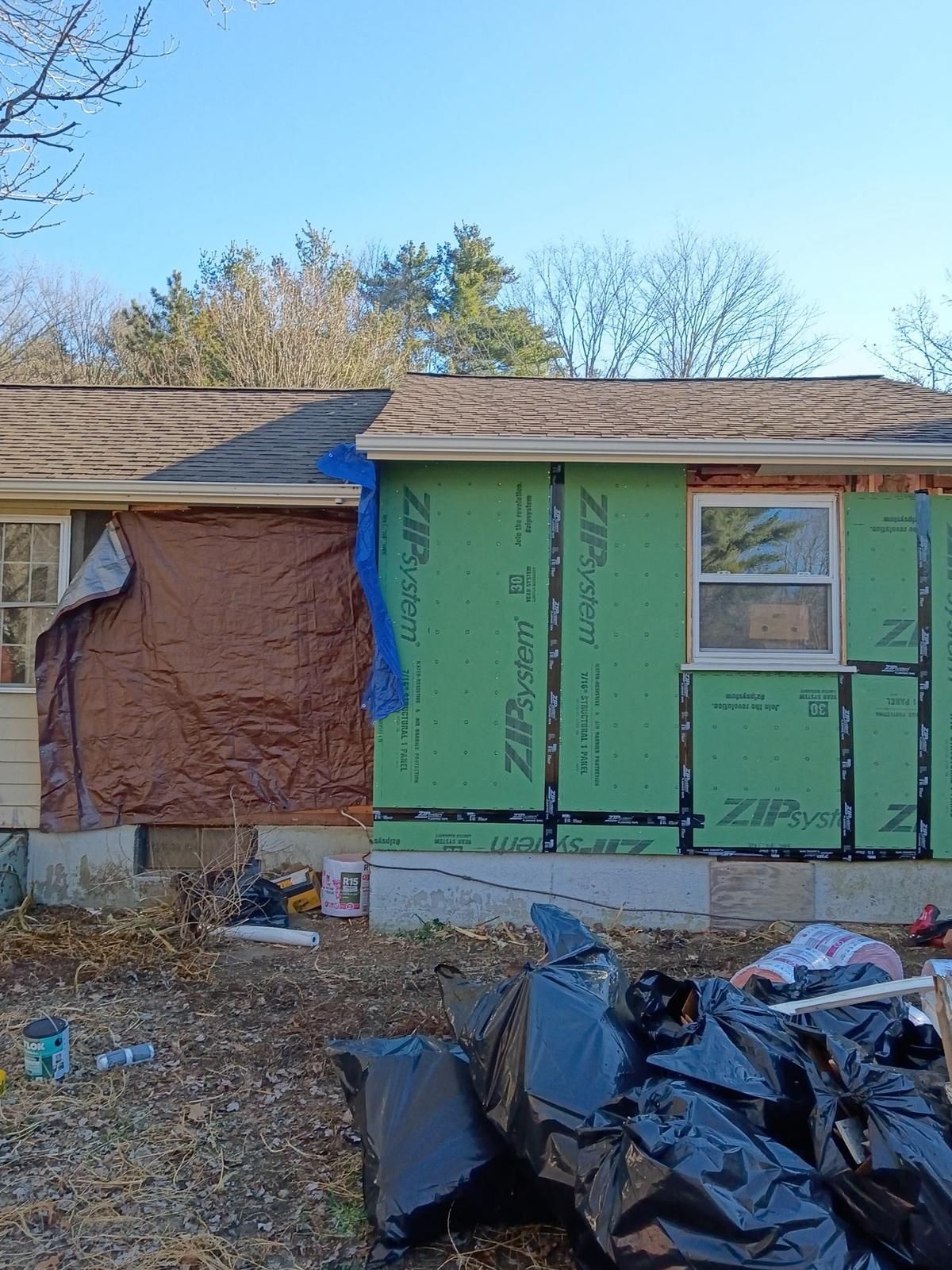 House exterior under renovation with green sheathing, brown tarp, and trash bags.