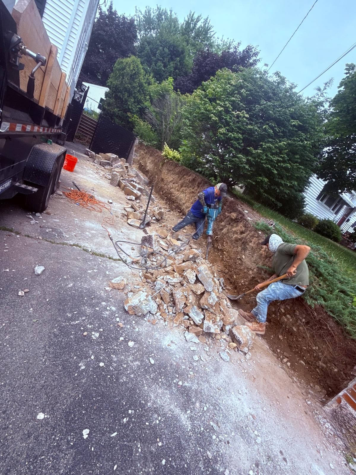 Two workers breaking down a retaining wall on a sloping driveway.