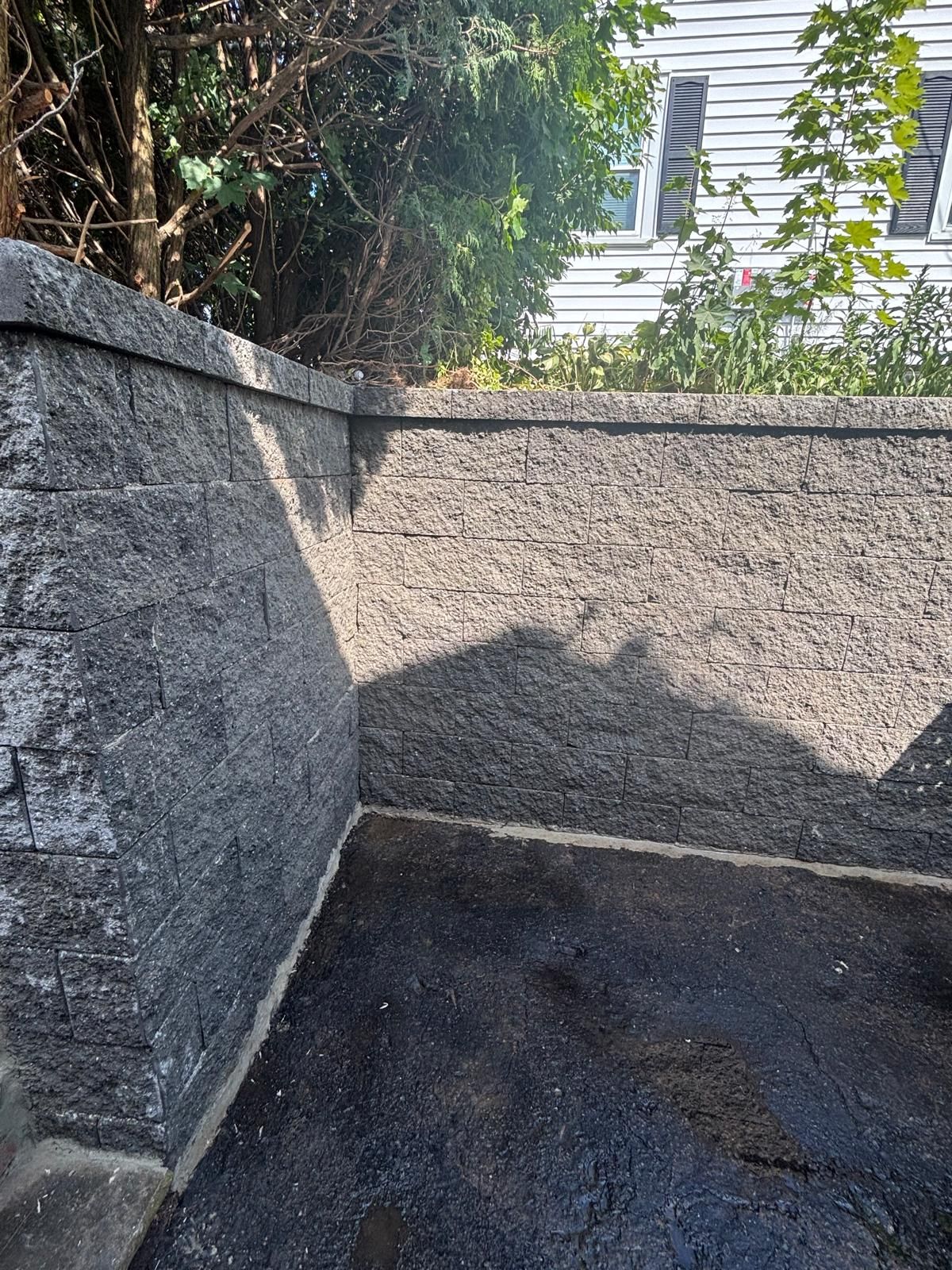 Stone retaining wall corner. Asphalt ground. Trees and building in background.