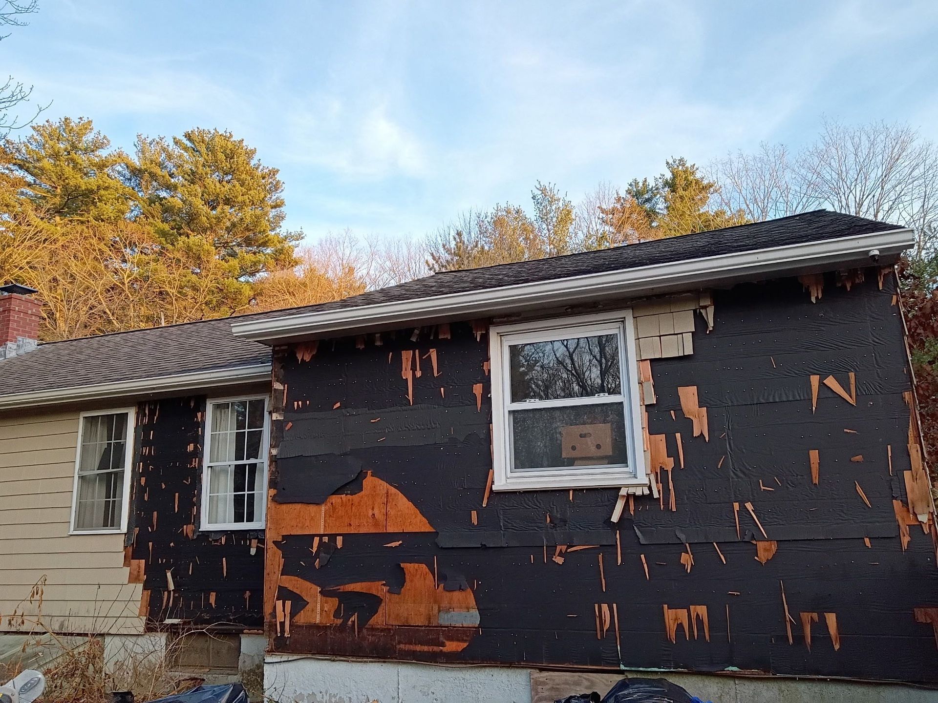 Exterior of a house with peeling black siding, white window frames, and weathered roof.