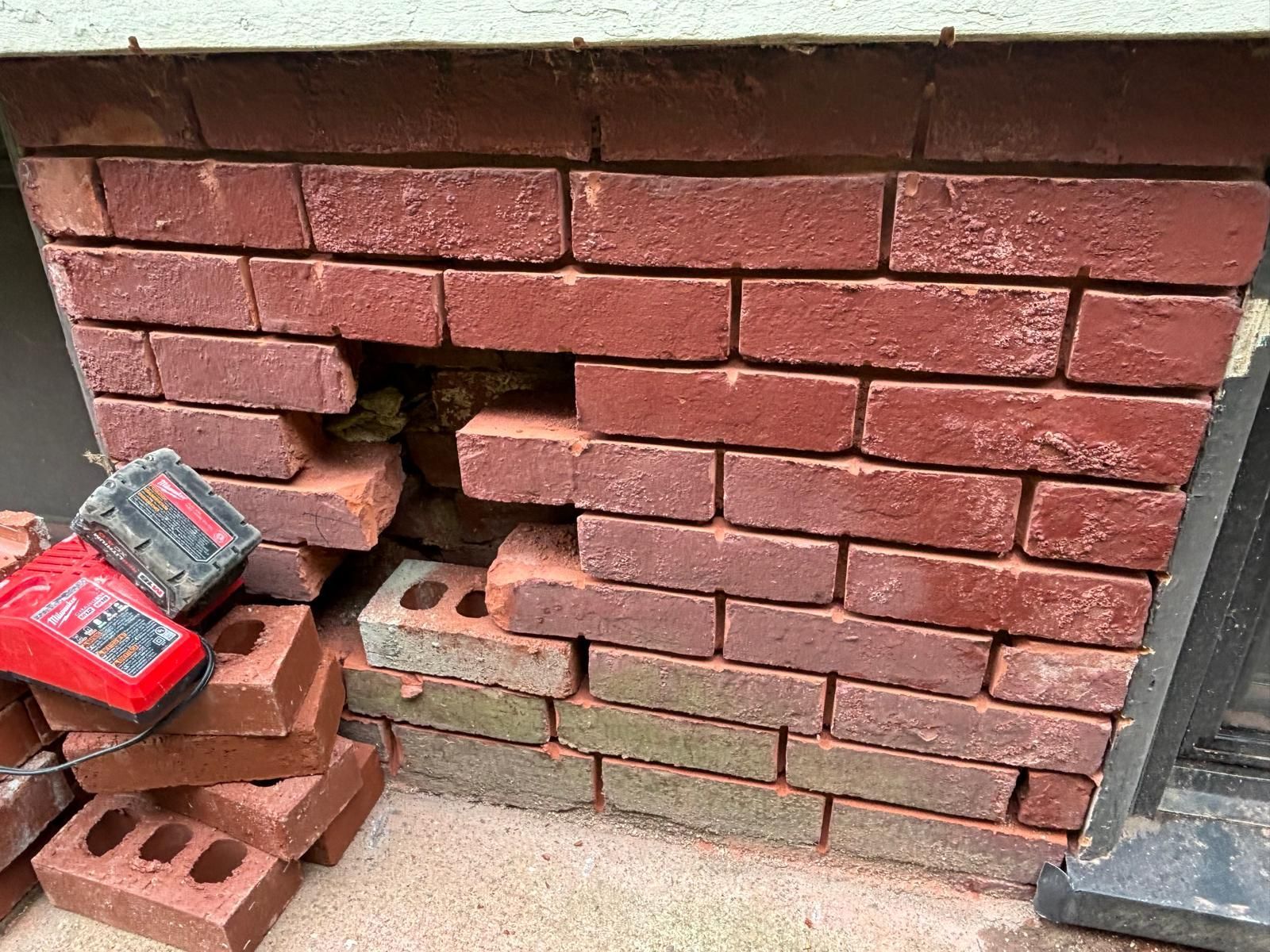 Damaged brick wall with missing bricks, revealing inner structure. Red bricks are piled nearby.