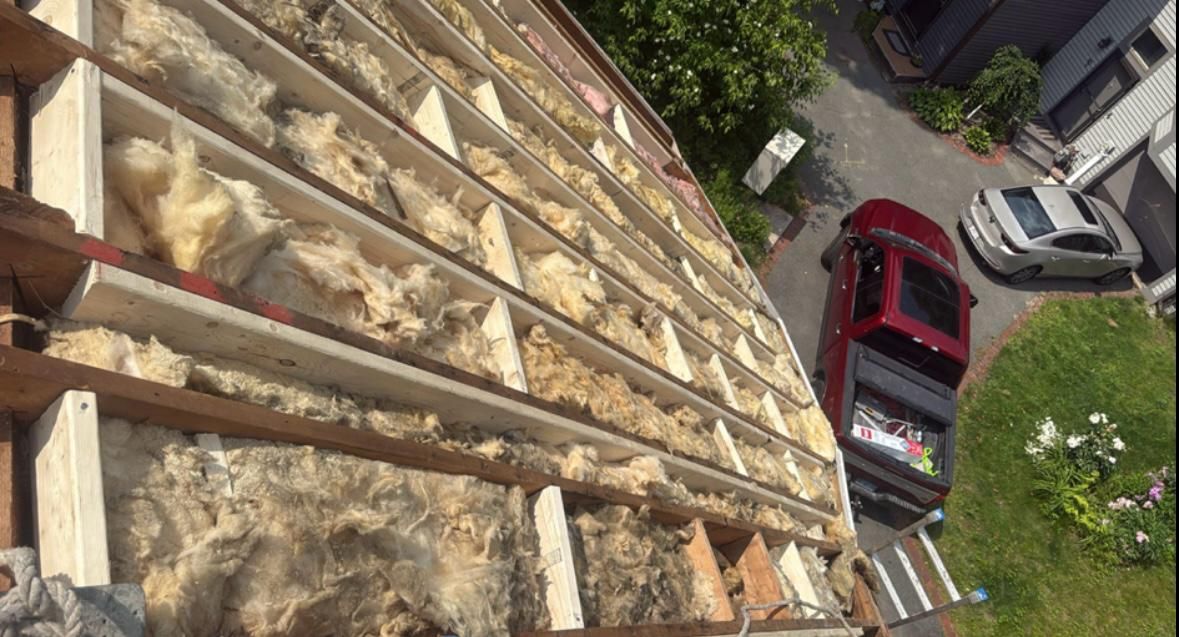Overhead view of a roof under construction; insulation installed between rafters; red truck and car parked nearby.