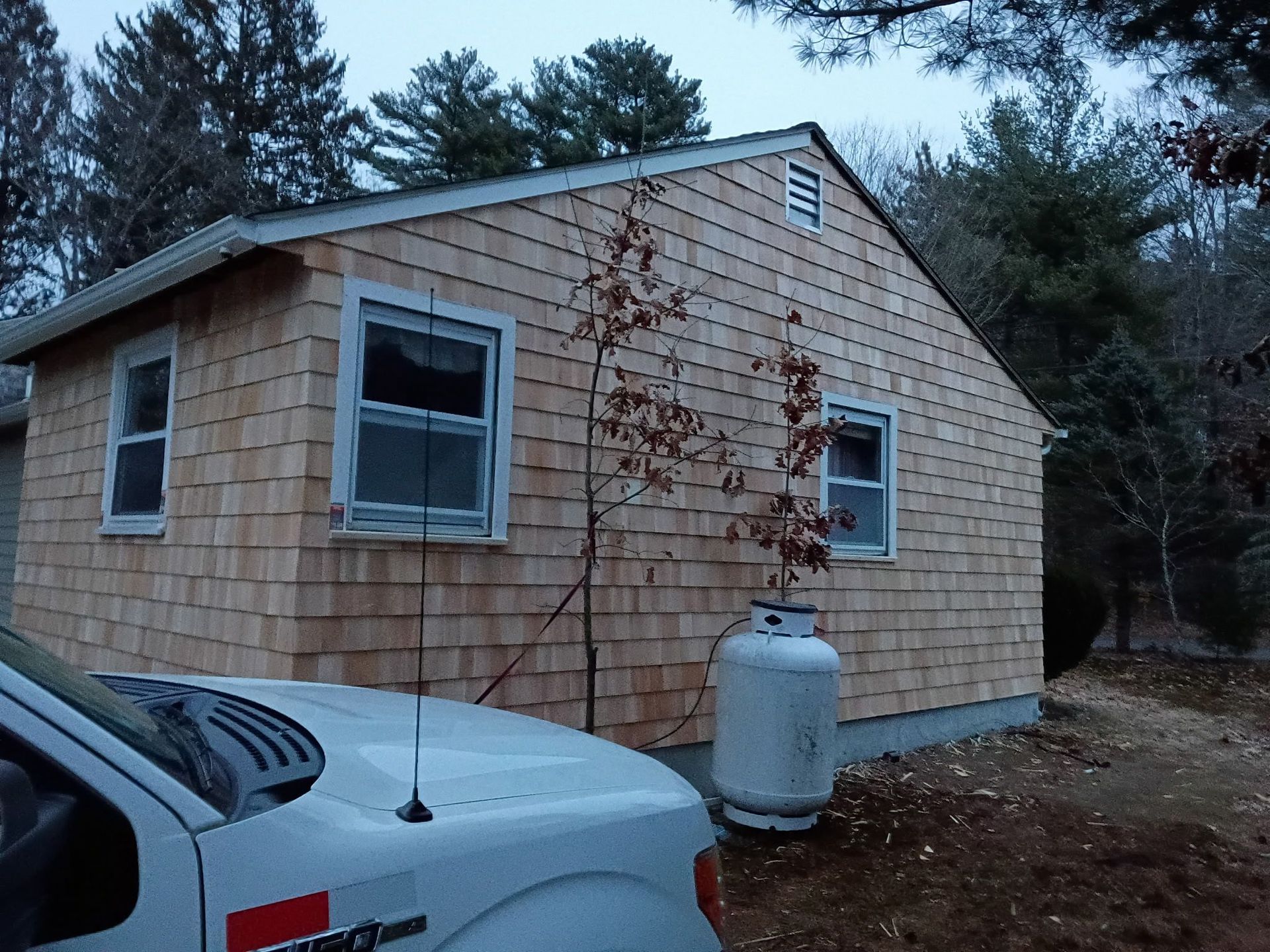 Wooden-shingled house with two windows, a propane tank, and a white truck in front.