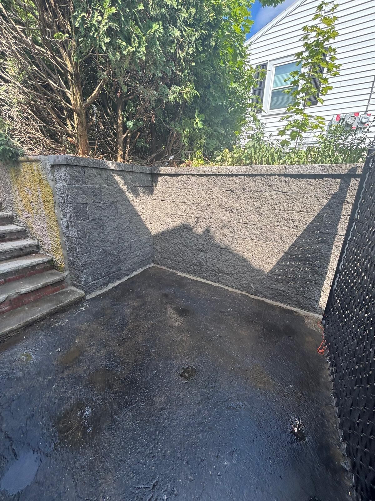 Asphalt paved area enclosed by a retaining wall with mulch, stairs, and a fence on the right.
