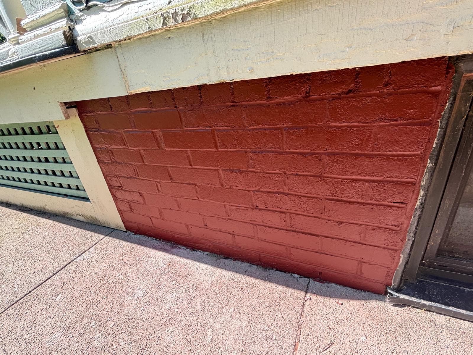Red painted brick foundation wall. Building corner with cream trim and ventilation.