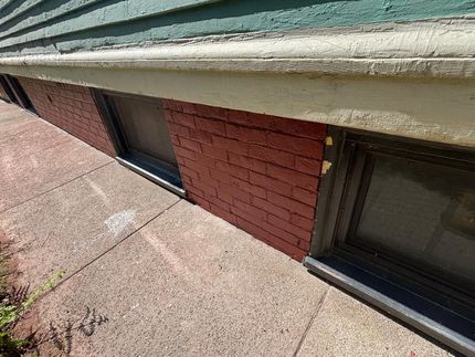 Brick facade with windows below a green and white building trim. Cement sidewalk.