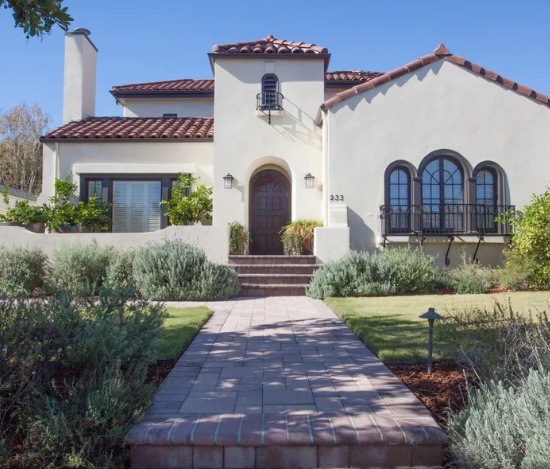 Spanish-style stucco house with red tile roof and arched windows, front walkway and garden.