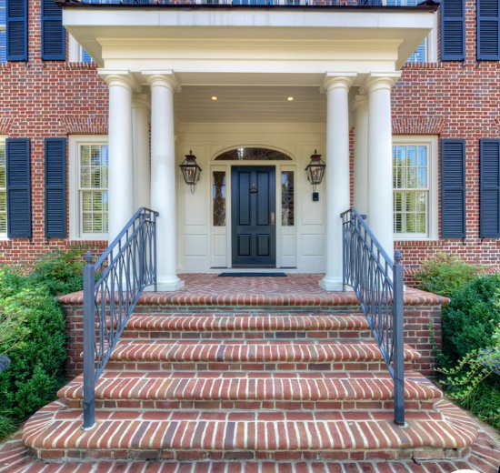 Brick front entrance with white columns, black door, and brick steps with black railings.