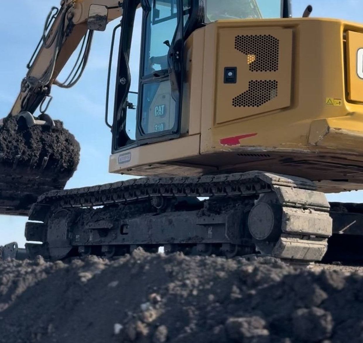 Yellow excavator scooping up dirt outdoors.