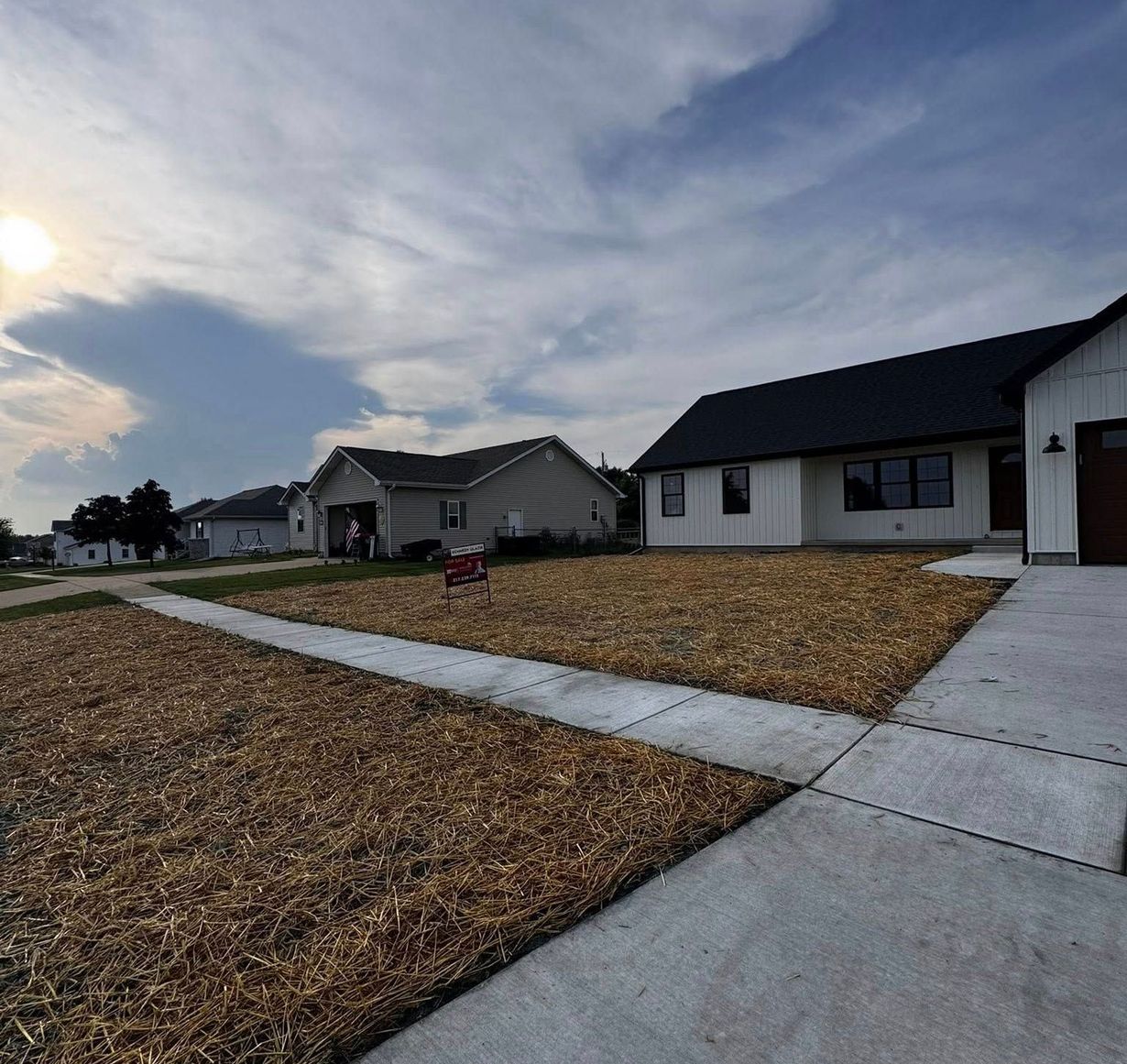 Residential houses with yards covered in mulch and a sidewalk on a cloudy day.