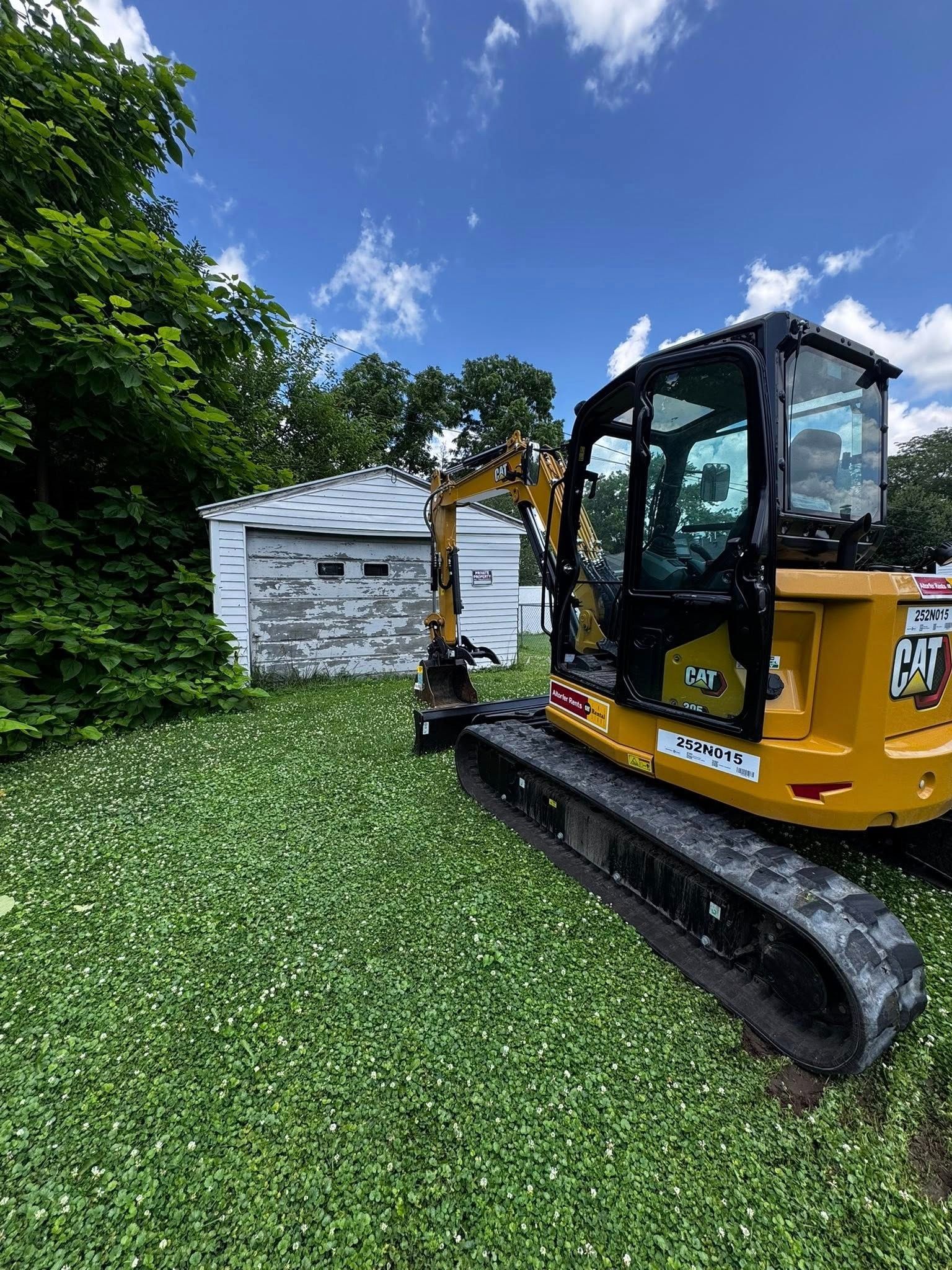 A yellow excavator is parked in a grassy yard in front of a garage.