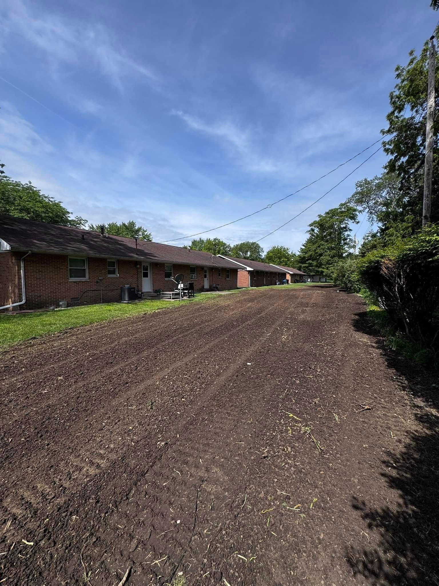 A dirt road leading to a house with a blue sky in the background.